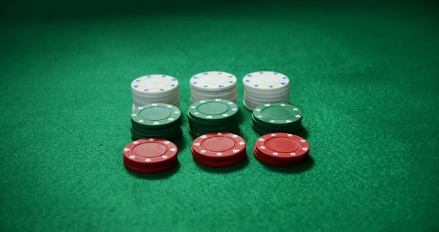 Stacks of red, green, and white poker chips arranged neatly on a green table. This visually appealing composition is ideal for illustrations related to gambling, high-stakes gaming, casino promotions, betting events, and gaming advertisements. The colors and organized presentation add to the feeling of excitement and competition often associated with casinos.