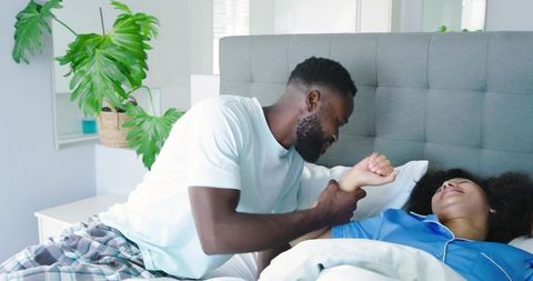 Black couple sharing morning laughter in cozy bed, playful wrist-hold, relaxed bedroom lifestyle