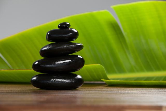 Stacked Black Pebble Stones on Wooden Table with Green Leaves - Download Free Stock Photos Pikwizard.com