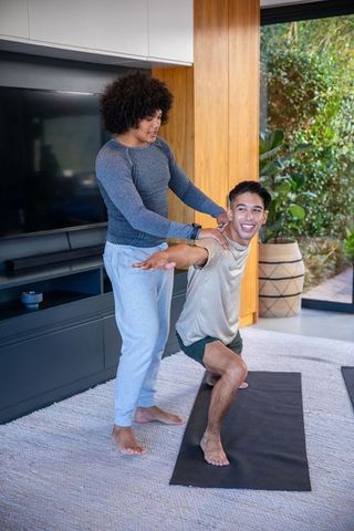 Yoga trainer assisting client in lunge pose for home fitness