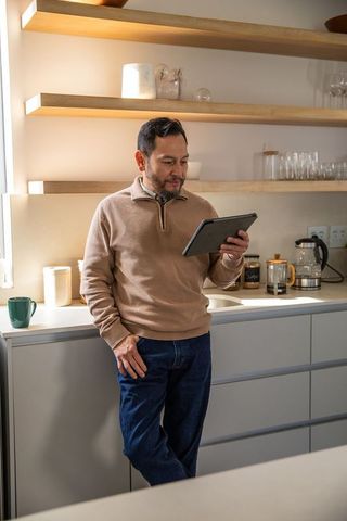 Middle-aged asian man reading tablet in modern minimalist kitchen, casual home technology