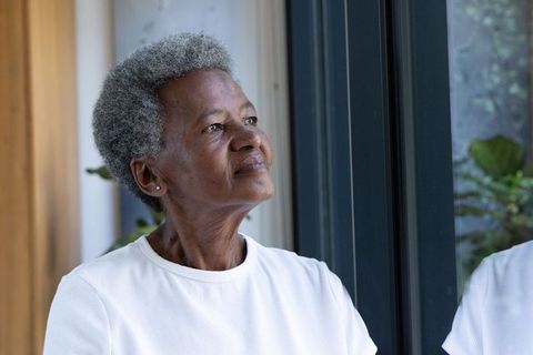 Senior african woman gazing out window in minimalist home, contemplative portrait