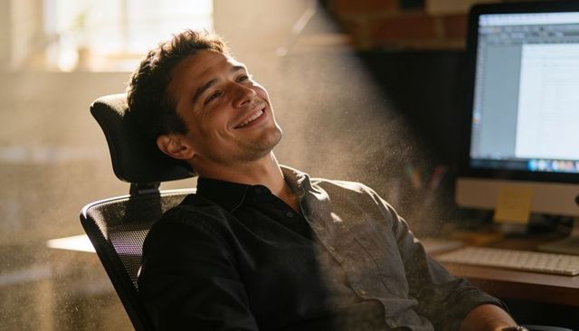 Young professional leaning back in ergonomic mesh chair smiling in sunlit loft workspace