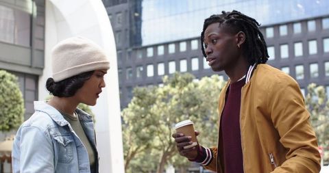 Young diverse friends talking and sipping coffee in urban plaza with glass architecture