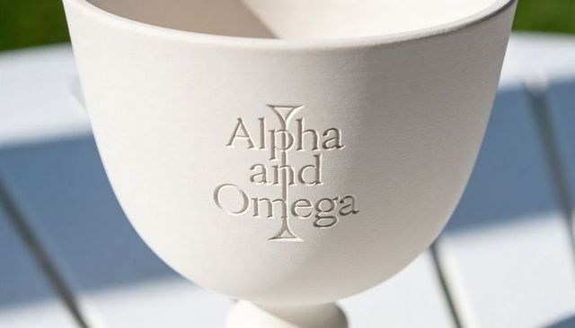 Sunlit white ceramic chalice embossed with alpha and omega cross, engraved goblet