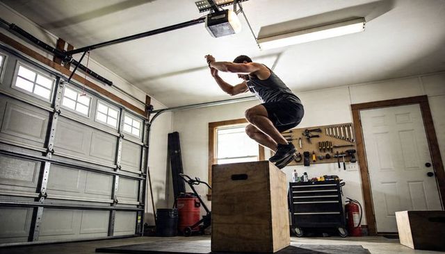 Athletic man performing explosive plyometric box jump in home garage gym workout