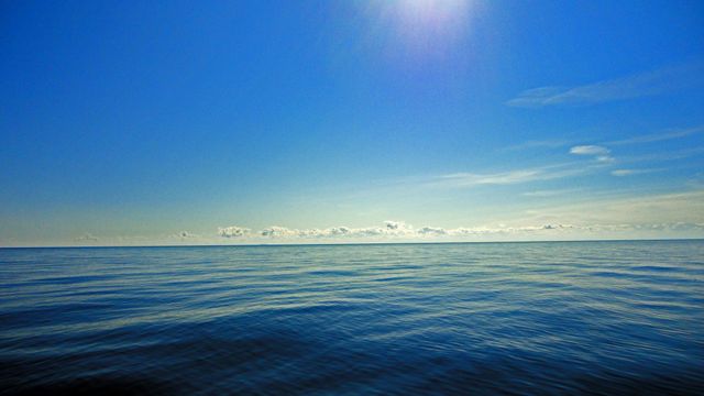 Calm open ocean with clear blue sky and gentle horizon. Perfect for themes like tranquility, nature, peacefulness, and outdoor activities. Suitable for backgrounds, travel promotions, relaxation and meditation materials.