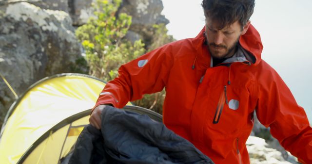 Caucasian man camping in wilderness preparing sleeping bag. Exploration, adventure, hiking, nature, hobbies, healthy lifestyle and outdoor activities, unaltered.
