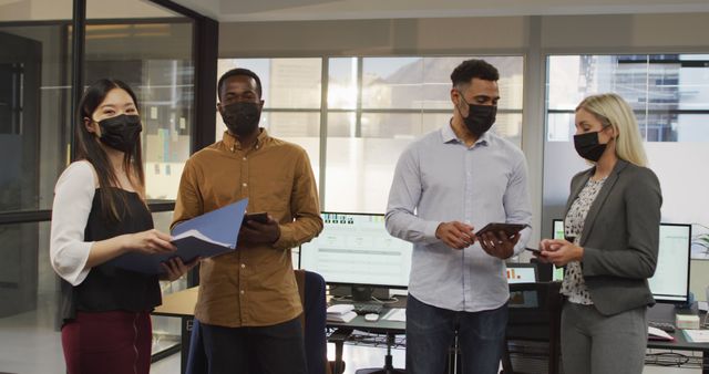 Group of diverse businesspeople wearing face masks and discussing together. work at a modern office during covid 19 coronavirus pandemic.