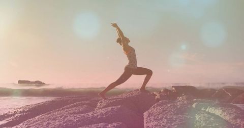 Sunrise coastal yoga lunge balancing woman stretching on rocky shore