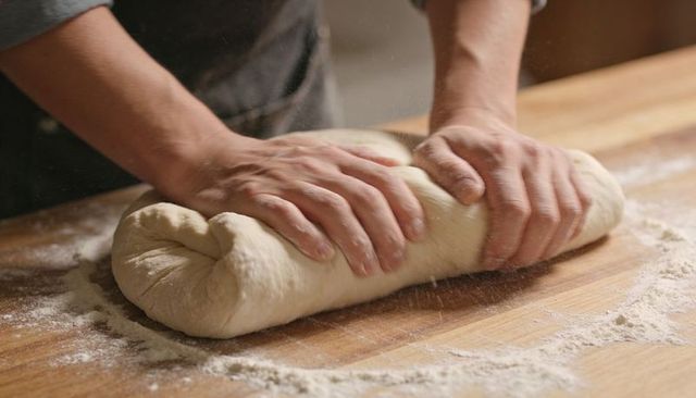 Artisan Hands Kneading and Rolling Rustic Bread Dough on Floured Wooden Workbench