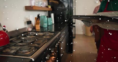 Baker Wearing Red Apron Carrying Tray Beside Stainless Gas Range and Oven