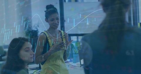 Leading woman presenting data in modern open-plan office with laptops and stock charts