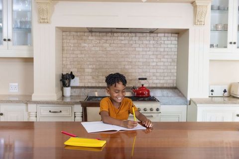Smiling african american boy doing homework at kitchen island with pencil and notebook