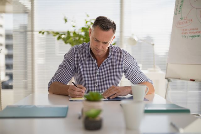 Male executive concentrating on paperwork in a modern office setting. Ideal for business, corporate, and productivity themes. Can be used for articles on office work, professional environments, and business strategies.