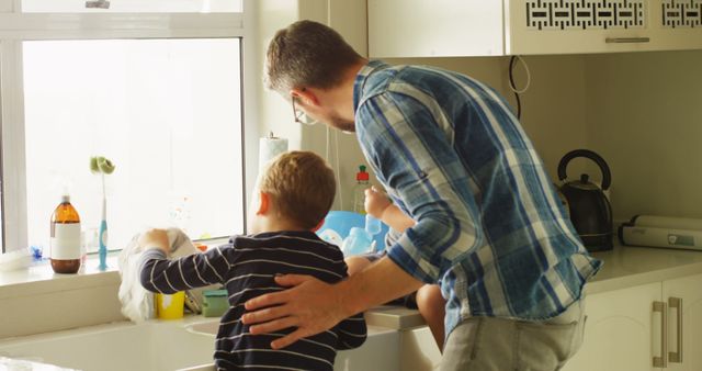 Caucasian man teaches a boy to wash dishes at home. They share a bonding moment while doing household chores together.