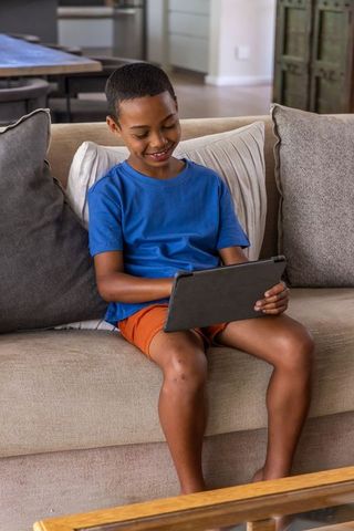 Smiling african american boy using tablet on sofa for learning and play at home
