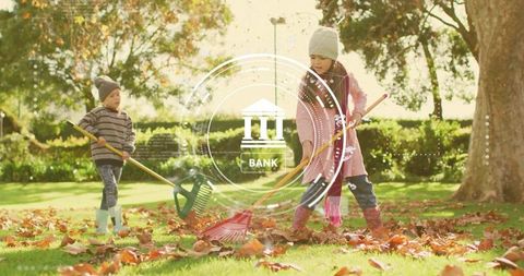 Siblings raking autumn leaves on sunlit lawn in park wearing knit hats and rain boots