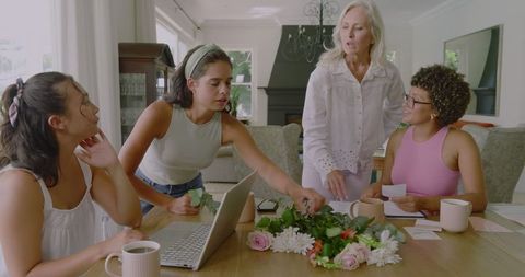 Diverse women discuss wedding planning ideas with flowers and laptop at home