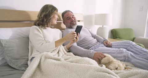 Mature Couple Relaxing in Bedroom with Smartphone and Pet Dog