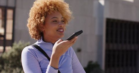 Young woman using voice assistant on smartphone outdoors in urban athletic outfit