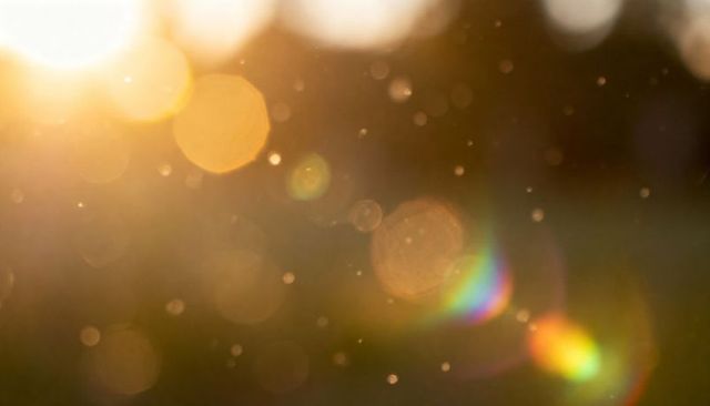 Shimmering golden bokeh and lens flare with prismatic rainbow and floating dust
