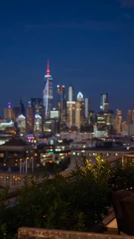 Vertical panning night skyline lowering to rooftop balcony plants and glowing bokeh