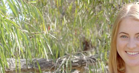 Woman Smiling Near Green Tree Branches in Sunlit Park
