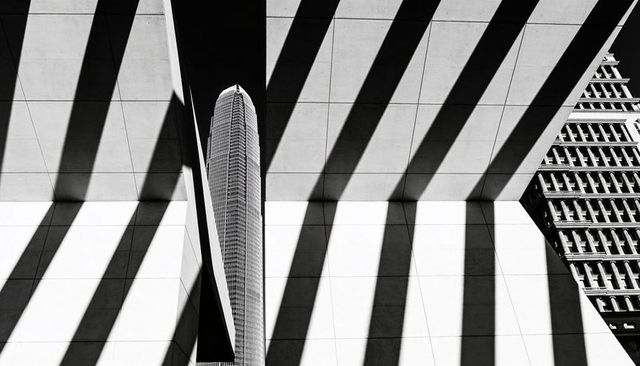Framed tower through concrete beams casting bold diagonal shadows in black and white