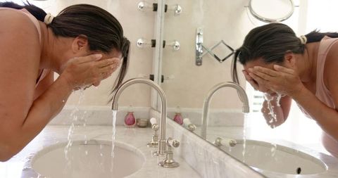 Woman washing face at bathroom sink for fresh skin