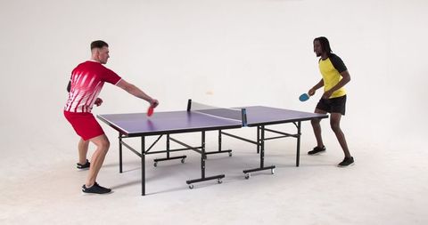 Two Diverse Friends Enjoying Competitive Table Tennis in Modern Studio