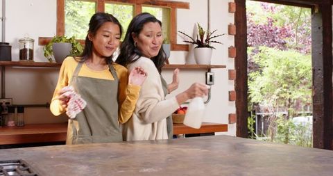 Mother and adult daughter cleaning kitchen together in cozy home