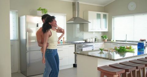Diverse couple embracing and laughing in modern sunlit kitchen with marble island