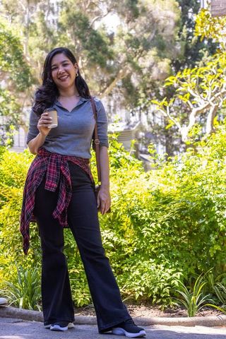 Smiling woman holding takeaway coffee standing in sunny urban park with casual street style