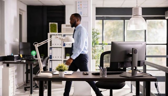 Businessman walking through modern open-plan office with minimalist desk, monitor and potted plant