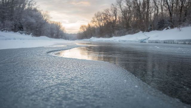 Curving frozen river reflecting soft sunrise in snow-covered winter valley