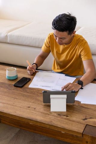 Young man reviewing paperwork at coffee table with tablet stand and mug, home workspace