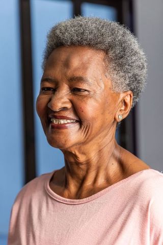 Senior african american woman smiling by window wearing pink top and stud earrings