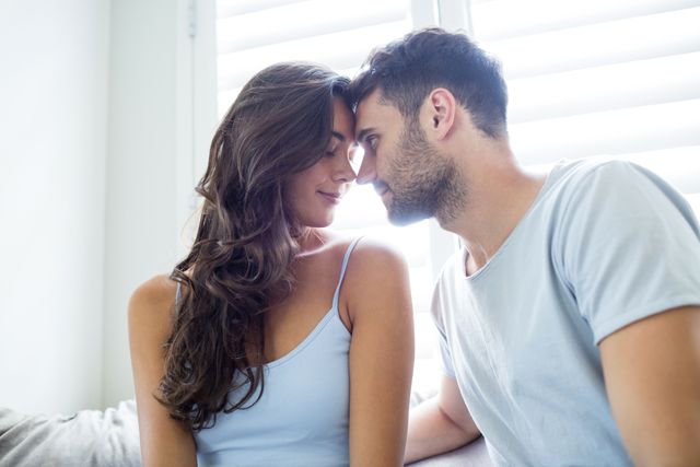 Young couple sharing an intimate moment in a cozy bedroom. Ideal for use in lifestyle blogs, relationship advice articles, romantic greeting cards, and advertisements promoting home decor or couple's products.