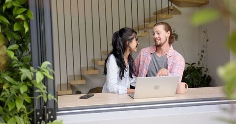 Diverse couple talking at laptop by home window