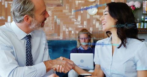 Business partners shaking hands in cafe over coffee with laptop, data overlays and collaboration