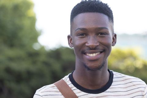 Smiling young man wearing striped shirt and crossbody bag outdoors