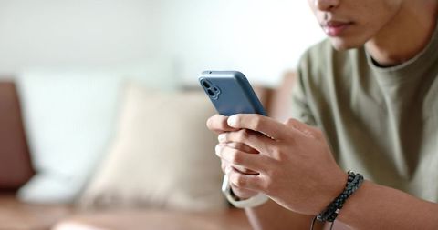 Young african american man holding smartphone on sofa wearing watch and braided bracelet