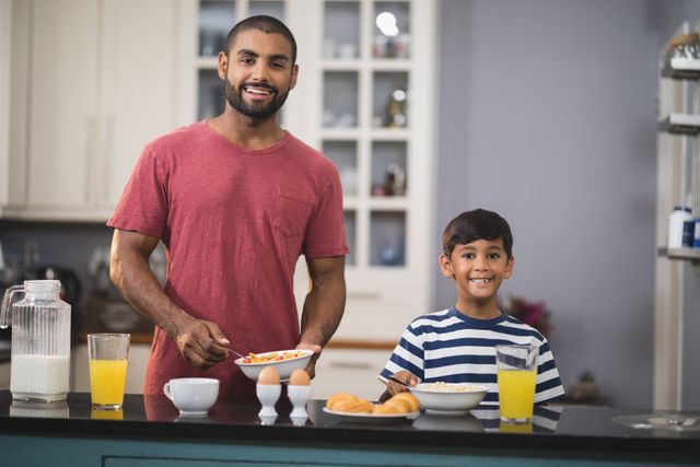 Father and son enjoying breakfast together in a modern kitchen. Ideal for use in family-oriented advertisements, parenting blogs, healthy eating promotions, and lifestyle articles focusing on family bonding and morning routines.