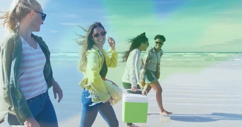 Friends walking on beach carrying cooler under bright sun, smiling and laughing