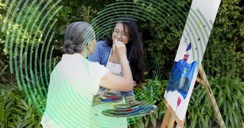 Senior artist teaching asian woman painting on easel in garden mentoring joyful creativity