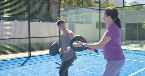 Women playing padel on blue court exchanging volleys in sunny outdoor match
