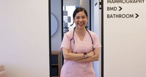 Smiling mammography nurse standing in clinic doorway wearing pink scrubs and stethoscope