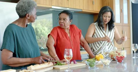 African american women cooking together at kitchen island preparing salad enjoying wine