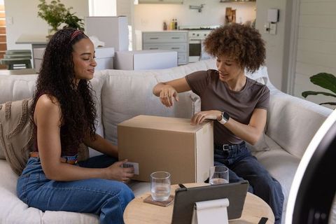 African american friends unboxing parcel on cozy living room couch for vlog and livestream